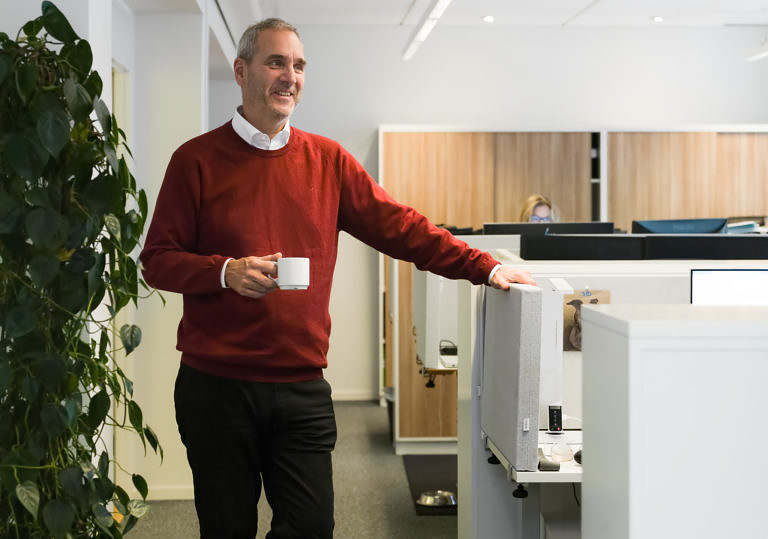 En man står bredvid ett kontorsbås med en kaffekopp i handen.
